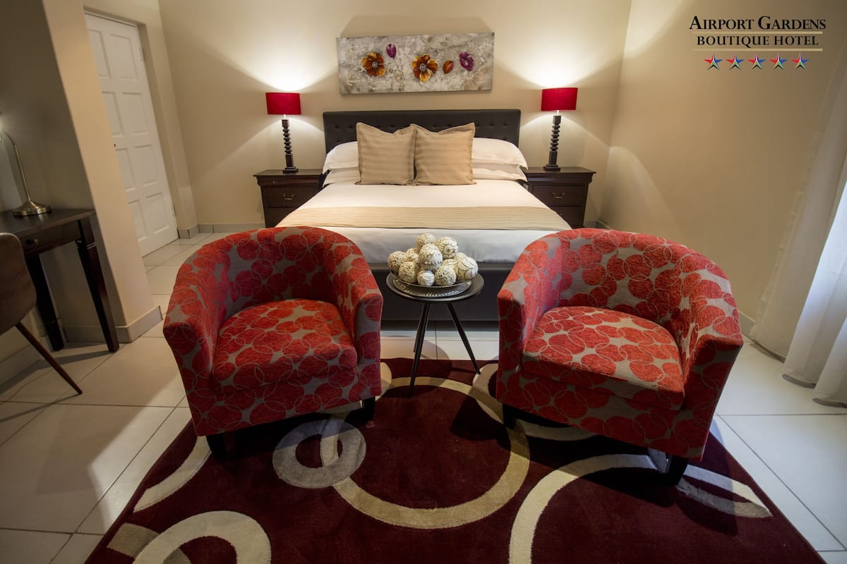 A hotel room with a bed, two armchairs, a small table with decorative items, and two bedside lamps.