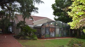 A greenhouse structure with glass walls, surrounded by a brick pathway and lush greenery.