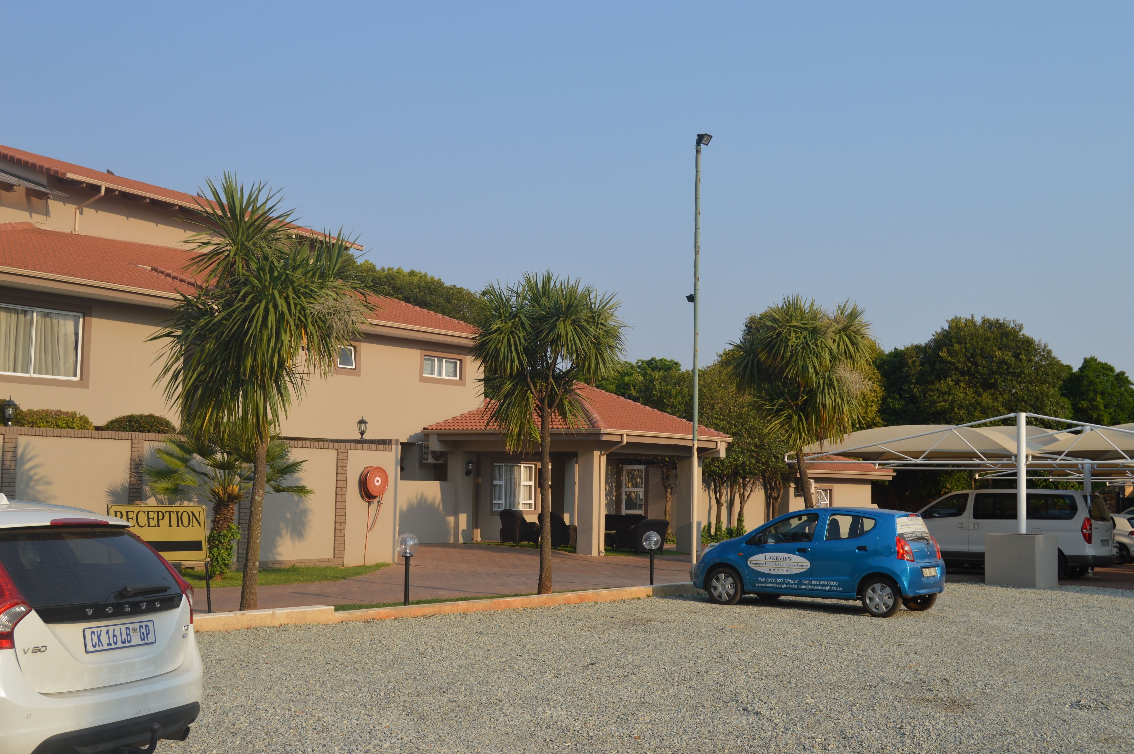 A building with a reception area, palm trees, and a parking lot with cars.