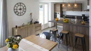 Una cocina moderna con una isla central, taburetes de bar, un reloj y un comedor con mesa y sillas.