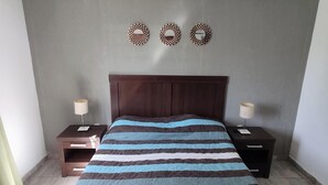 Een slaapkamer met een bed, twee nachtkastjes en drie spiegels aan de muur.