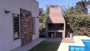 Een modern huis met een gevel van natuursteen, een zwembad en een barbecueplaats.