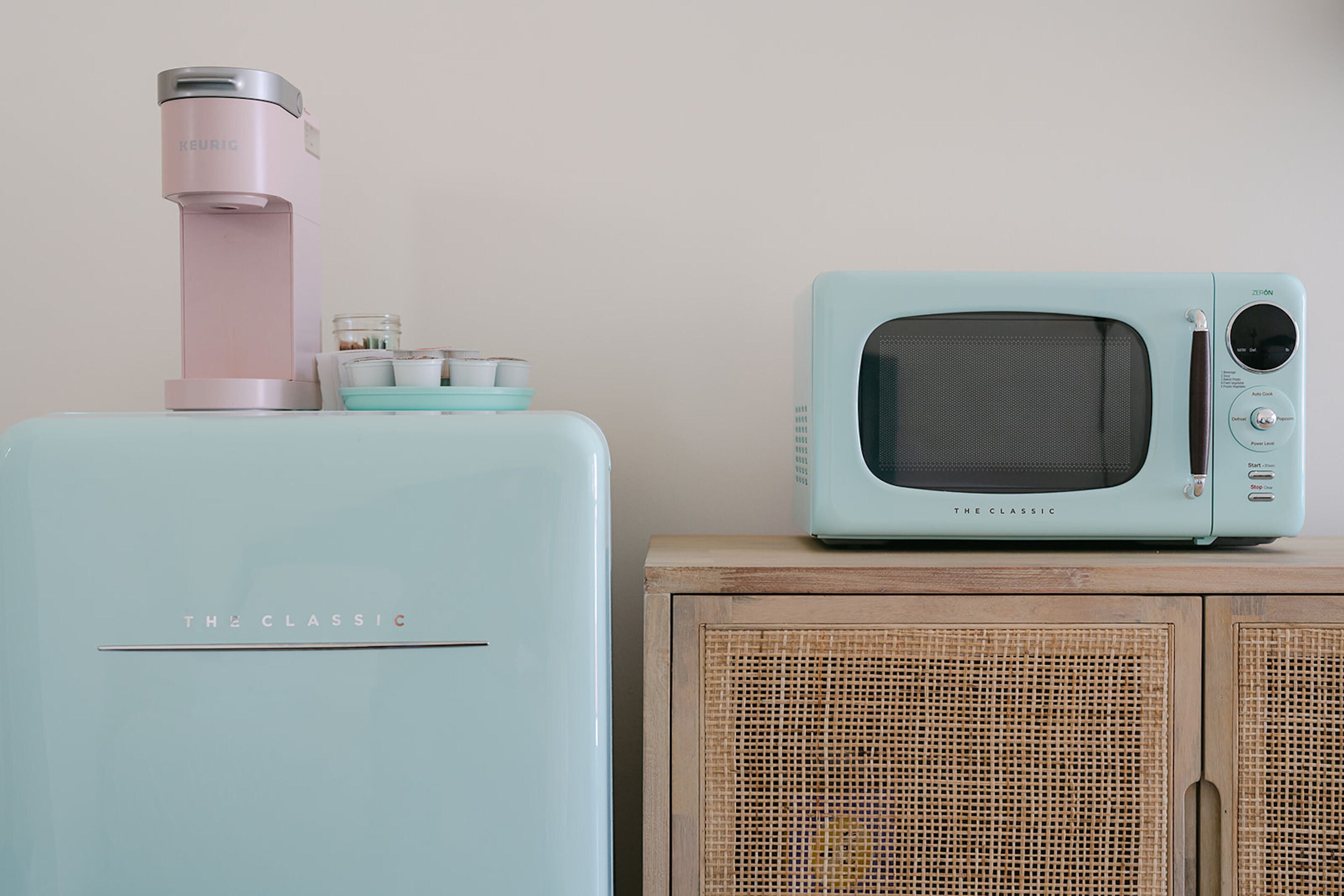 Un frigorifero color acquamarina con un erogatore d'acqua rosa e un forno a microonde in stile retrò sopra.