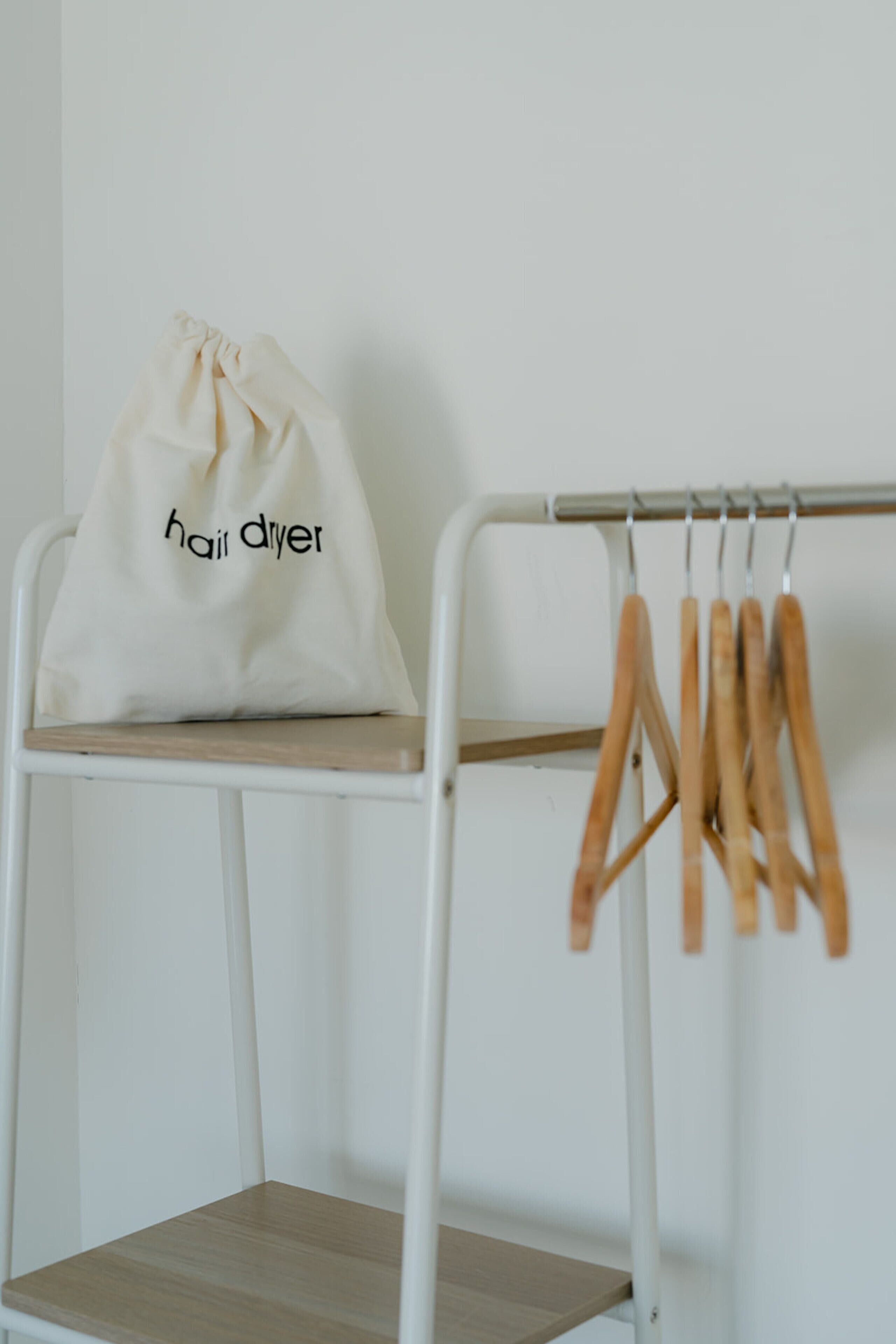 A white metal chair with a white bag labeled "hair dryer" on top and wooden hangers on a metal rack.