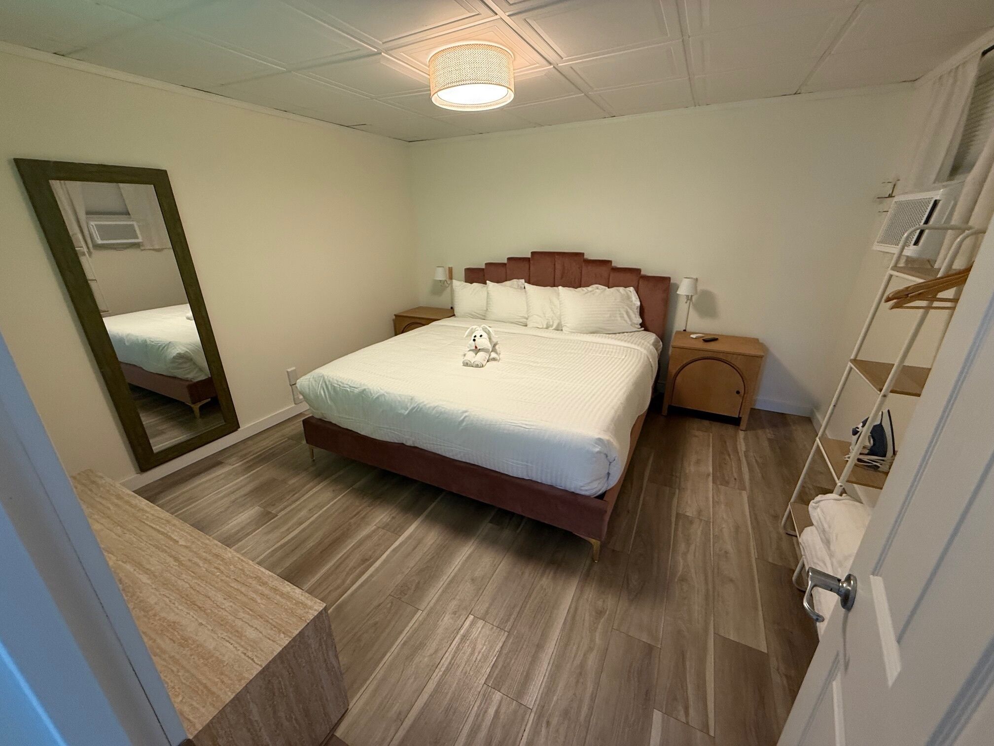 Un dormitorio ordenado con una cama grande, una mesita de noche, un armario y un espejo.