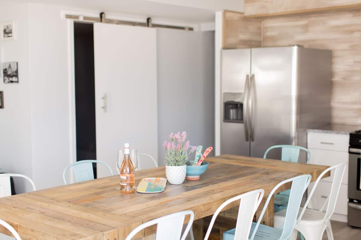 Una mesa de madera con sillas, un cuenco de flores y una botella de agua.