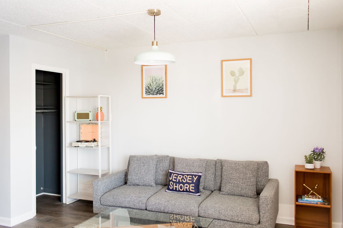 Una sala de estar moderna con un sofá gris, una lámpara colgante blanca y una estantería.