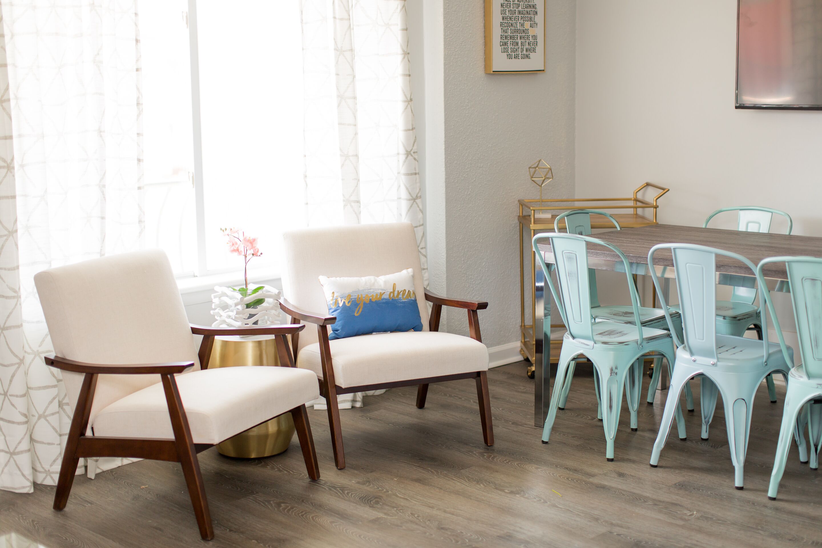 A dining area with a wooden table and chairs, a small side table with a plant, and a wall with a framed quote.