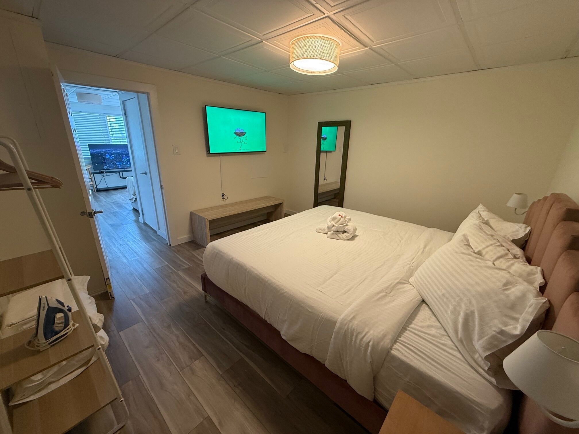 A hotel room with a bed, a TV mounted on the wall, a bench, and a wooden floor.