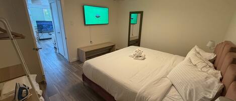 A hotel room with a bed, a TV mounted on the wall, a bench, and a wooden floor.
