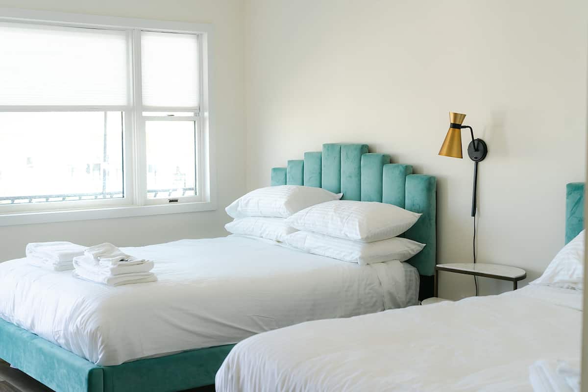 Habitación de hotel con dos camas, una ventana y una mesita de noche con lámpara.