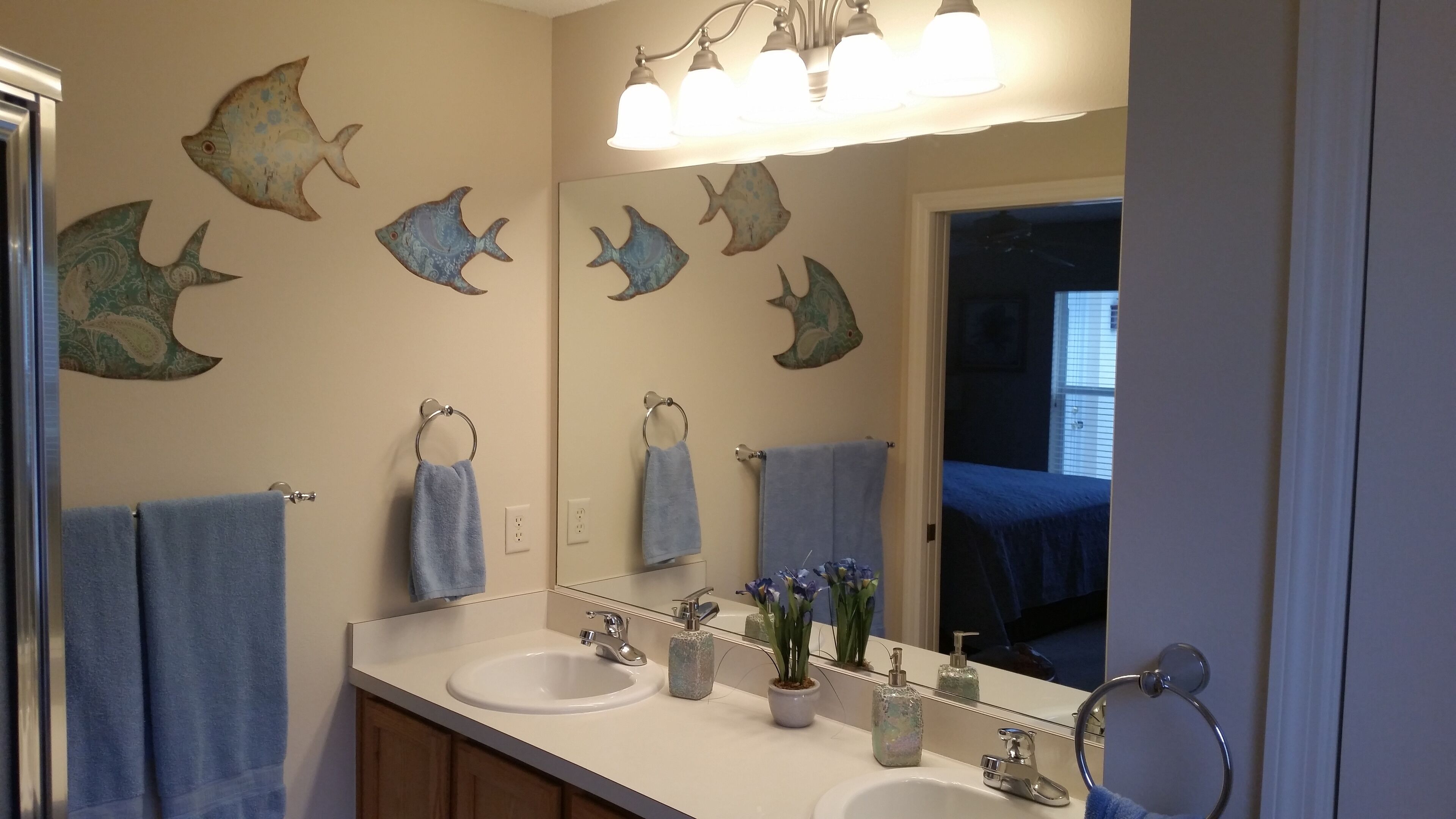 A bathroom with two sinks, a mirror, and decorative fish wall art.