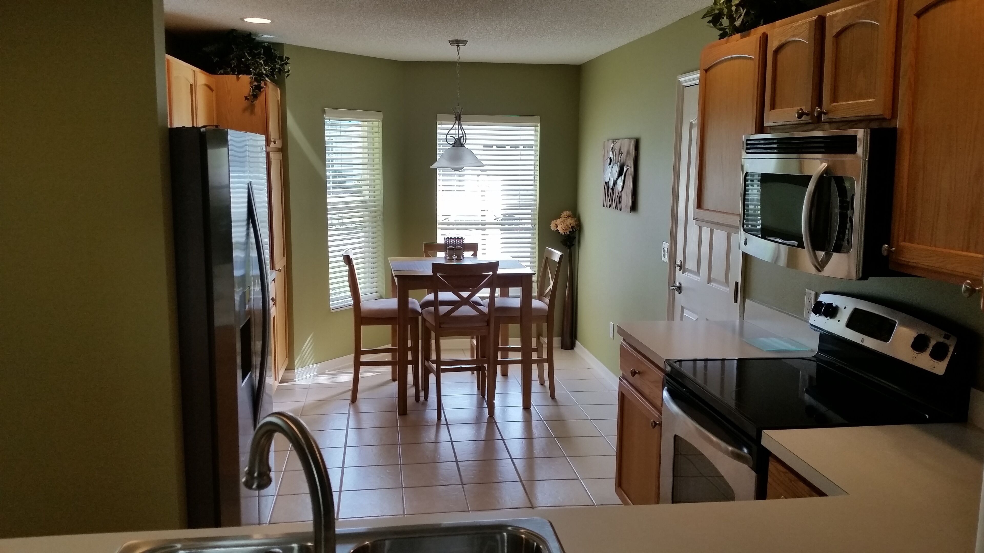 Una cocina con armarios de madera, un refrigerador, un microondas y una mesa de comedor con sillas.
