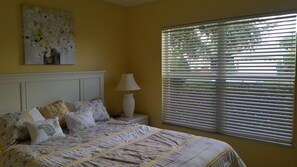 A bedroom with a bed, a nightstand, a lamp, and a window with blinds. -  Walk to Lake Sumter Landing! Golf cart included! (The Villages)
