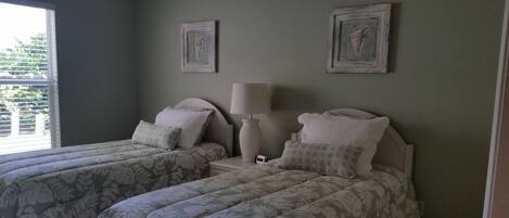 A bedroom with two beds, each with floral-patterned bedding, a bedside table with a lamp, and two framed pictures on the wall.
