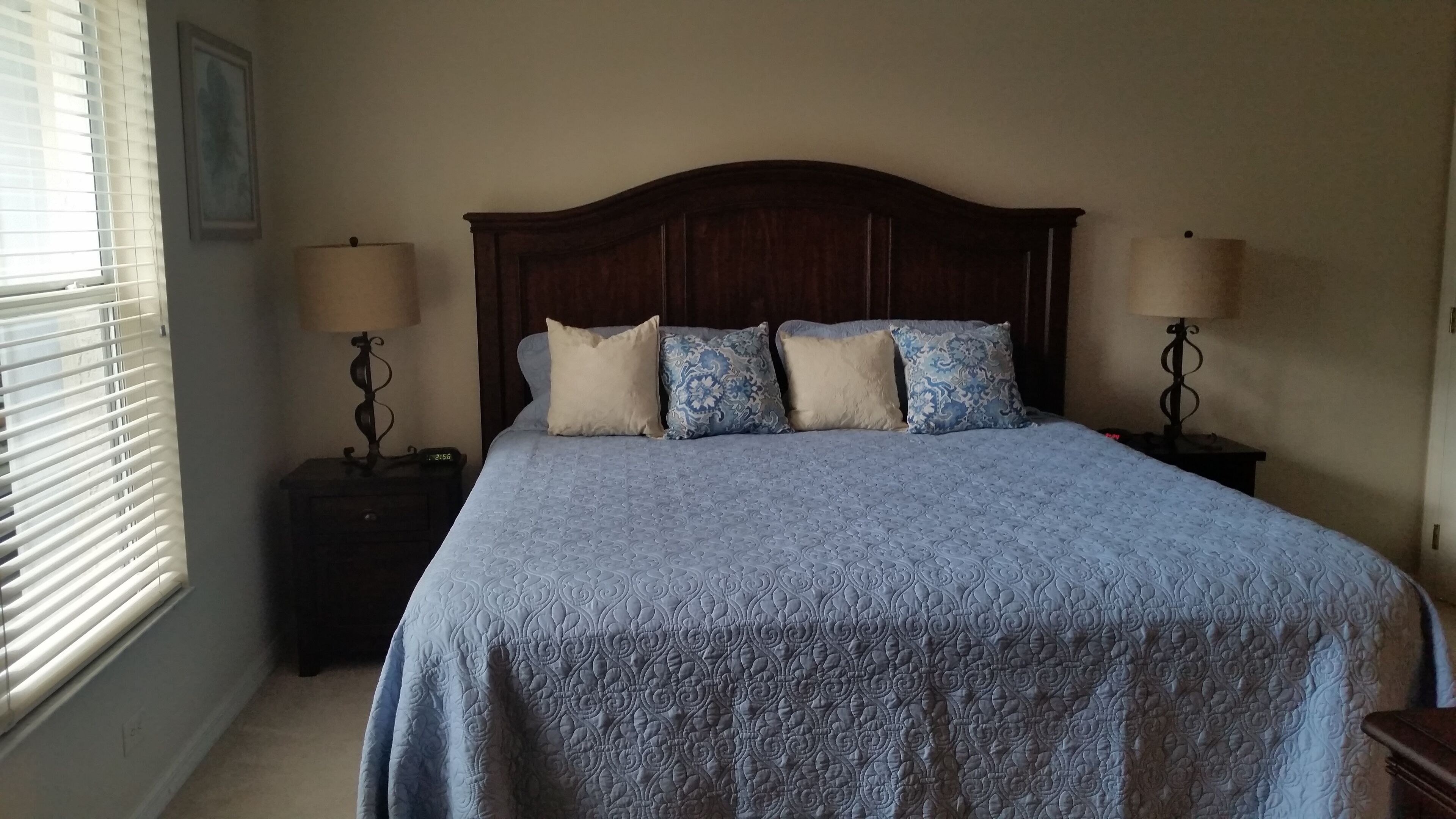 A bedroom with a large bed, two bedside tables, and a window with blinds.