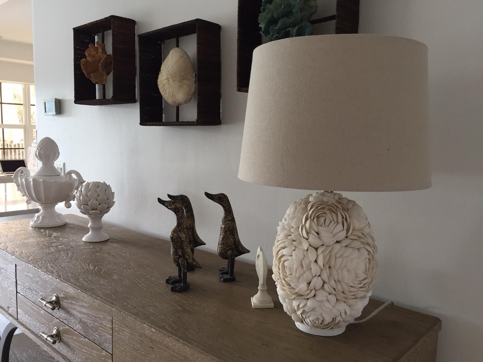 A wooden dresser with decorative items including a white vase, two bird figurines, and a textured lamp.