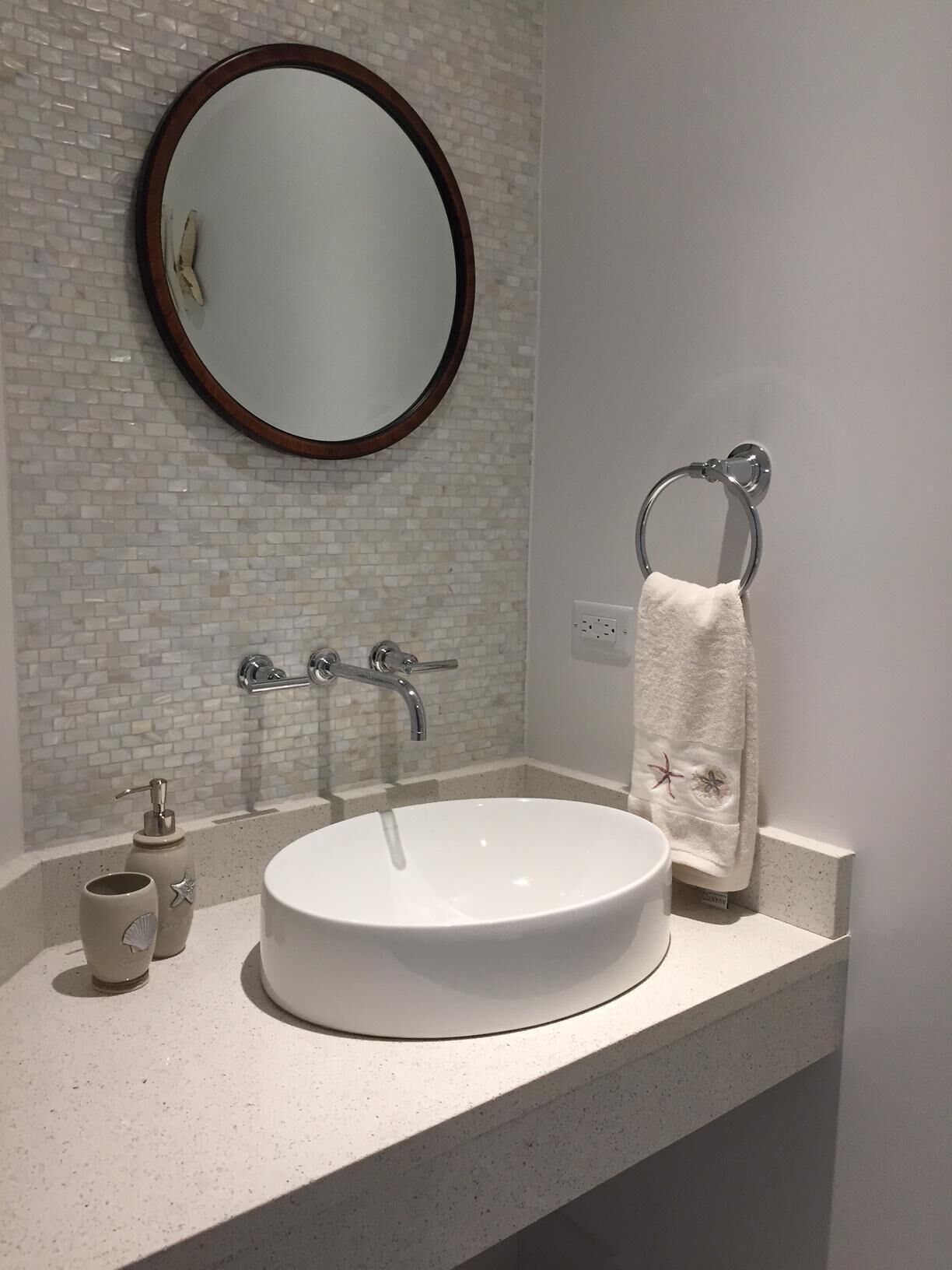 Un baño con un espejo redondo, un lavabo blanco, un aro para toallas y un dispensador de jabón.