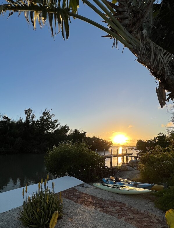 A sunset view over a calm lake with a dock and kayaks.