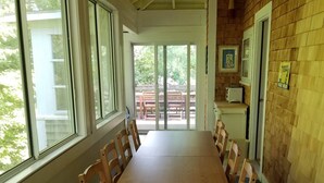 A long wooden dining table with chairs, large windows, and a brick wall. - Charming Cape House in Megansett area of North Falmouth - walk to the beach! (North Falmouth)
