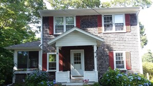 A two-story house with a front porch, red shutters, and a number 7 on the side. - Charming Cape House in Megansett area of North Falmouth - walk to the beach! (North Falmouth)