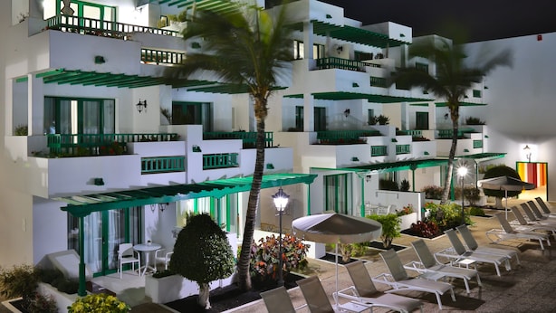 A multi-story hotel with balconies, outdoor seating, and palm trees. - Nazaret Apartments (Teguise)