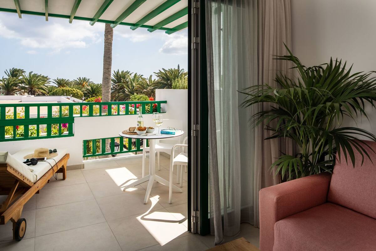 Ein Balkon mit einem weißen Tisch, Stühlen, einem Holzstuhl und einer pinkfarbenen Couch.