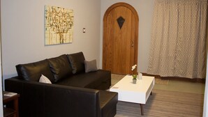 Ein Wohnzimmer mit einem dunkelbraunen Ledersofa, einem weißen Couchtisch, einer Holztür und einem gemusterten Vorhang.