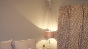 Ein Schlafzimmer mit Bett, Nachttisch, Lampe, Deckenventilator und einem gemusterten Vorhang.