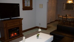 Ein Wohnzimmer mit Flachbildfernseher, Kamin, weißem Couchtisch und einer Essecke mit einer Kristallleuchtre.