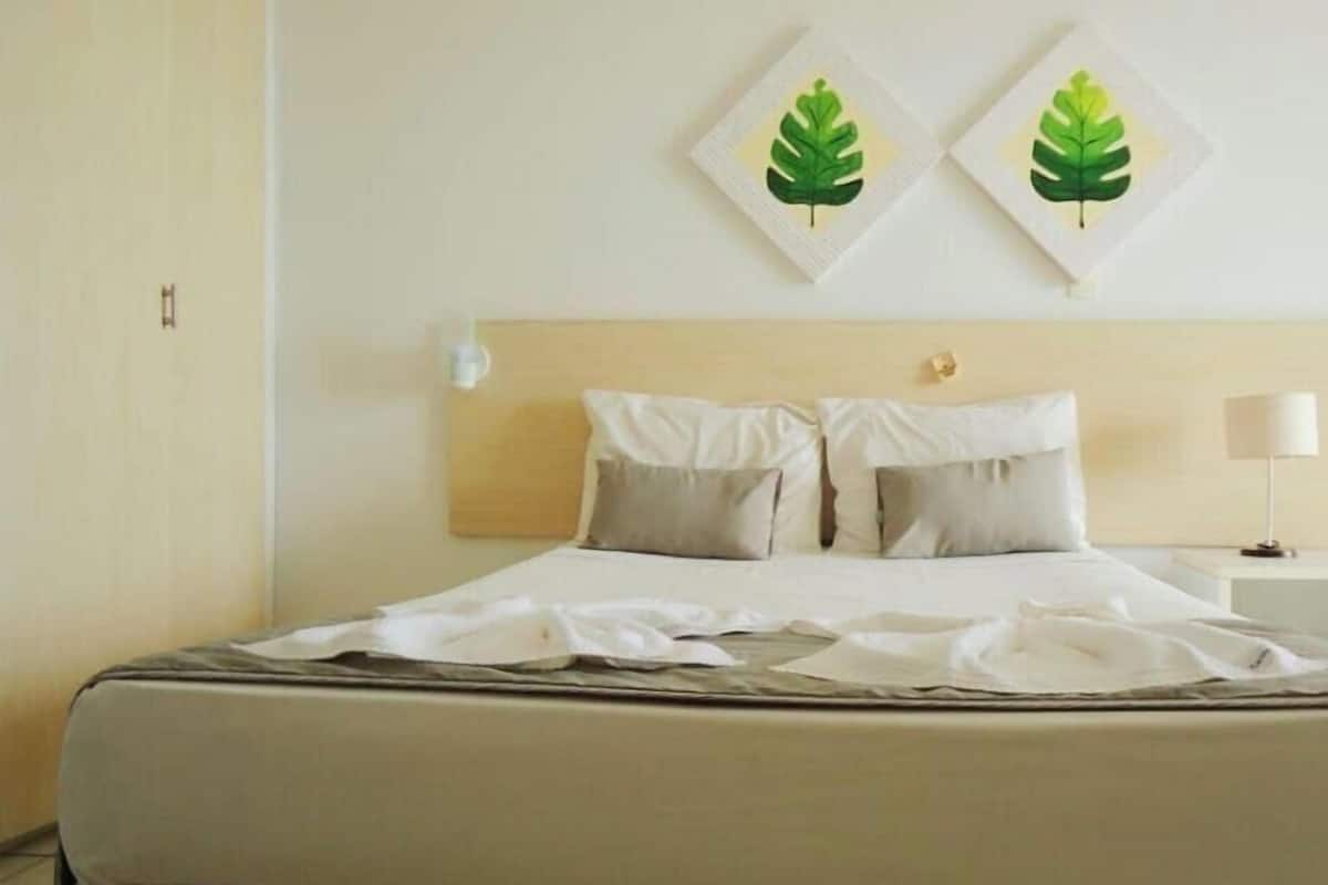 Ein ordentlich bezogenes Bett mit weißen Leinen, einem Holzkopfbrett und zwei an der Wand aufgehängten Blätterbildern.