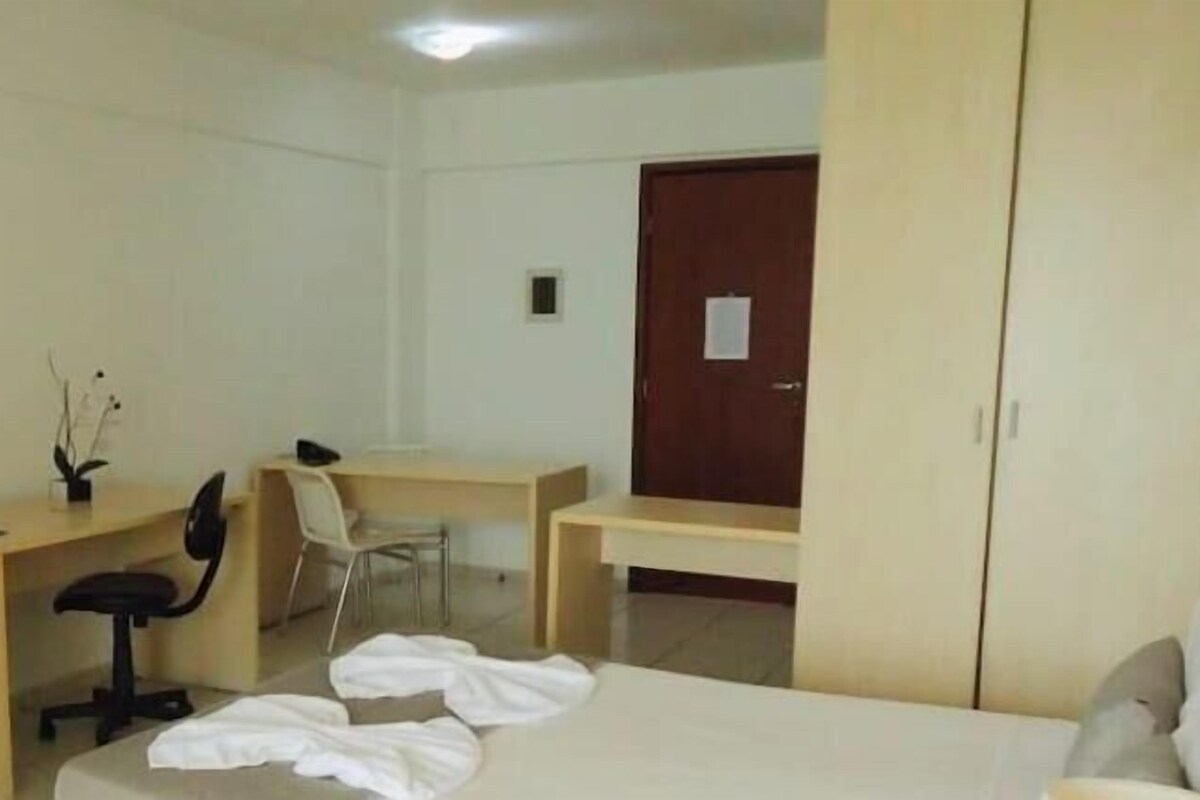A hotel room with a bed, a desk with a chair, a television, and a wardrobe.