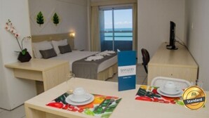 Een hotelkamer met een bed, een bureau, een eettafel gedekt met borden en een kaart, en uitzicht op de oceaan door het raam.
