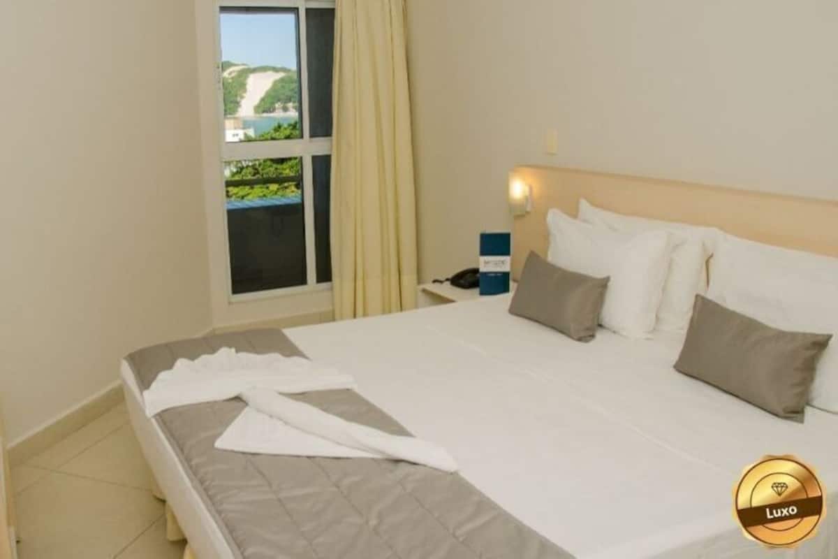 Ein Hotelzimmer mit Bett, Fernseher, Fenster mit Vorhängen und Nachttisch mit Lampe.