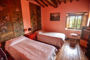 A bedroom with two beds, a red suitcase, a small stool, and a window with a view of greenery. - Charming Tuscany Villa with magical Garden, shared pool,  Chianti Area  (Castelnuovo Berardenga)