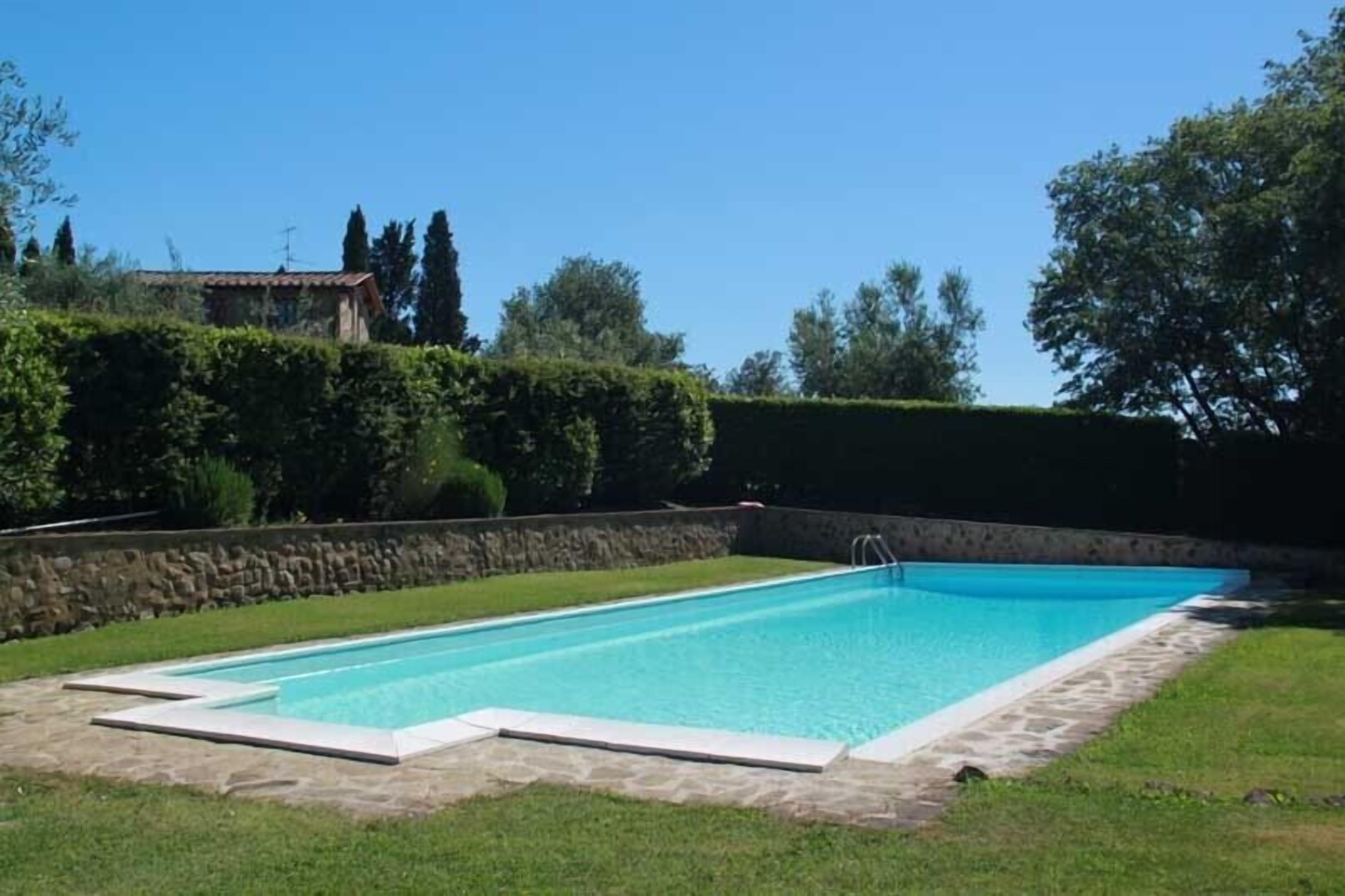 Ein rechteckiger Pool mit Steinbordstein, umgeben von einer Steinmauer und einer Rasenfläche.