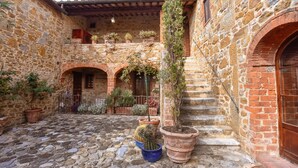 A courtyard with stone walls, potted plants, and a staircase leading to an upper level. - Charming Tuscany Villa with magical Garden, shared pool,  Chianti Area  (Castelnuovo Berardenga)