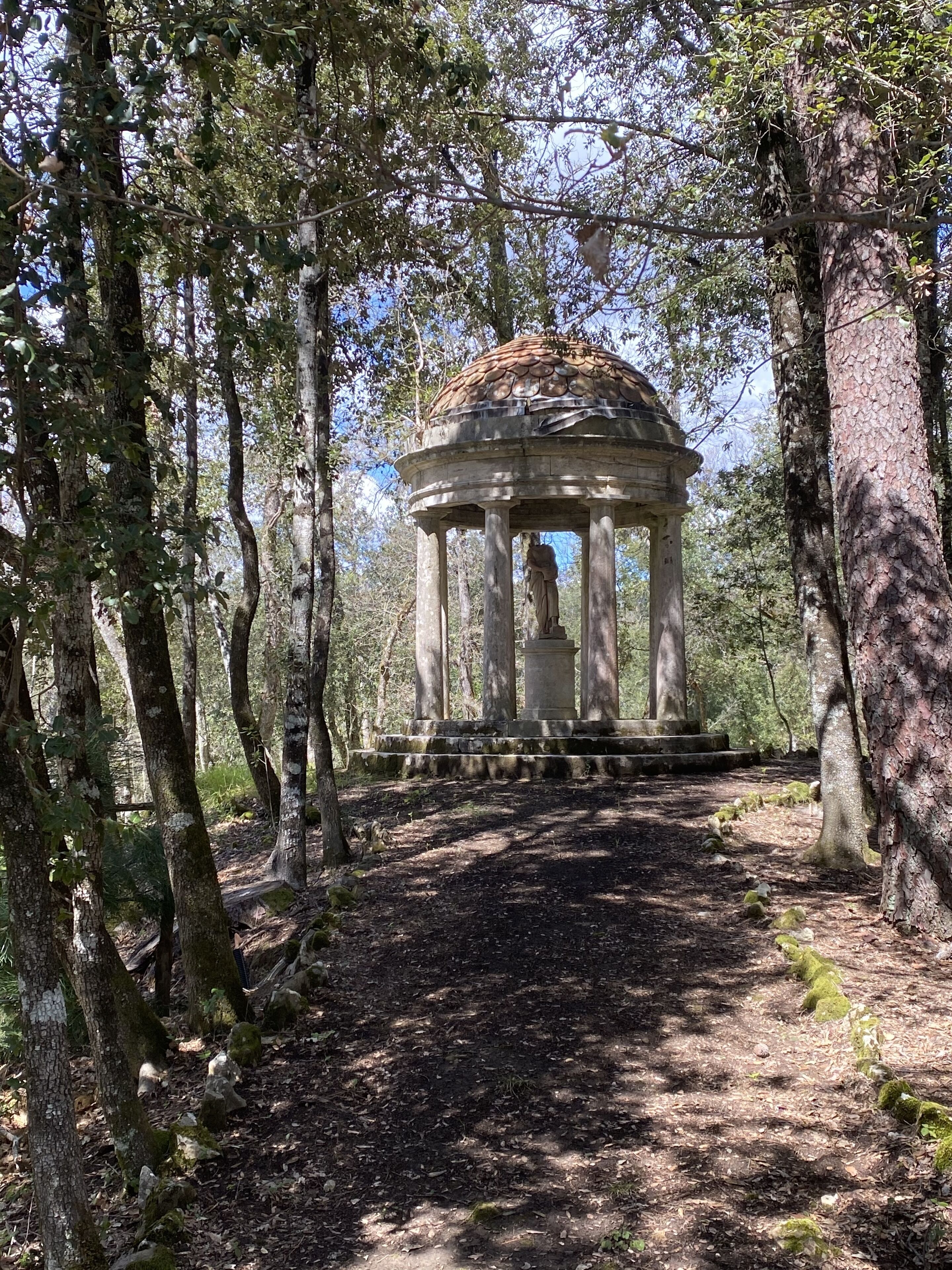 A gazebo in a forested area with a dirt path leading to it.