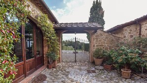 A stone courtyard with a wooden pergola, potted plants, and a metal gate. - Charming Tuscany Villa with magical Garden, shared pool,  Chianti Area  (Castelnuovo Berardenga)