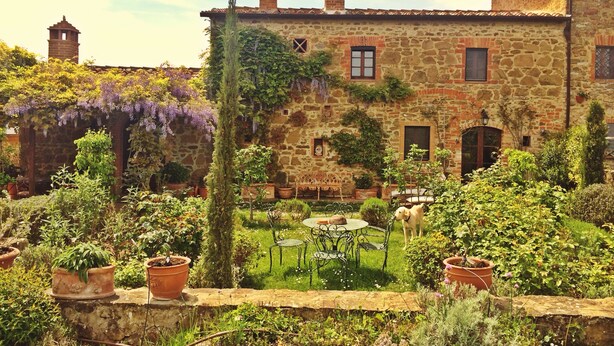 A stone building with a garden, a small table with chairs, and a dog. - Charming Tuscany Villa with magical Garden, shared pool,  Chianti Area  (Castelnuovo Berardenga)