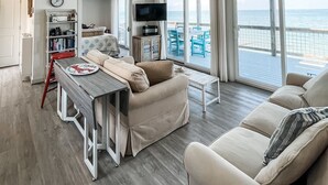 A spacious living room with a ceiling fan, a dining area with a table and chairs, a bookshelf, and a large window overlooking the ocean. - Modern Beachfront Cottage with Endless Bay Views (Port Haywood)