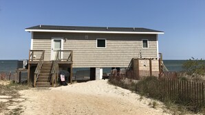A beach house with a sandy driveway leading to a wooden deck. - Modern Beachfront Cottage with Endless Bay Views (Port Haywood)