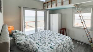 A bedroom with a bed, a ceiling fan, a window with a view of the sea, and a ladder leaning against the wall. - Modern Beachfront Cottage with Endless Bay Views (Port Haywood)