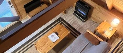Ein Interieur einer Holzhütte mit einem Bett, einem kleinen Tisch, einem Stuhl und einem Schreibtisch mit einem Computer.