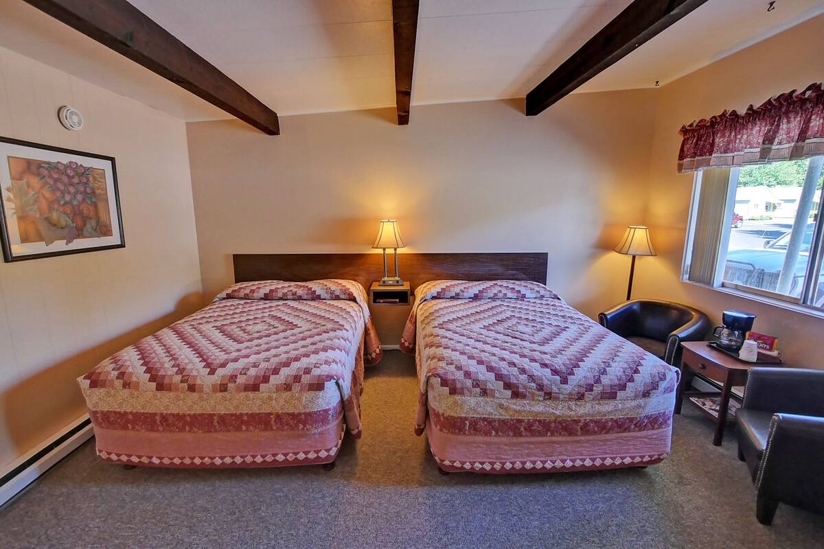 A room with two beds, a chair, a small table, and a window with curtains.