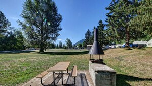 A picnic area with a table and benches, a barbecue grill, and a view of a campground with cabins and a mountain in the background. - Idle A While (Twisp)