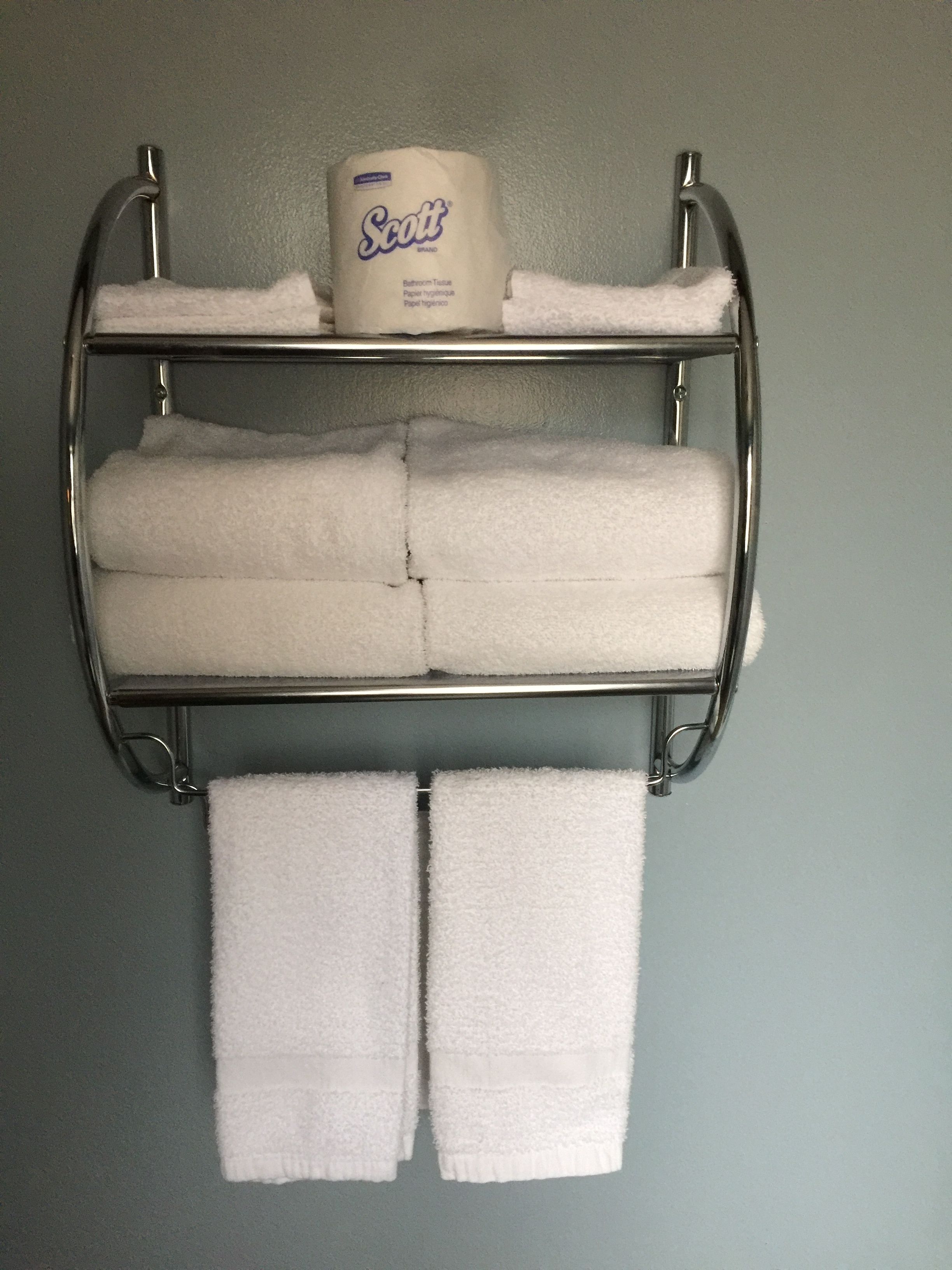 A metal towel rack with three folded white towels and a Scott toilet paper roll.