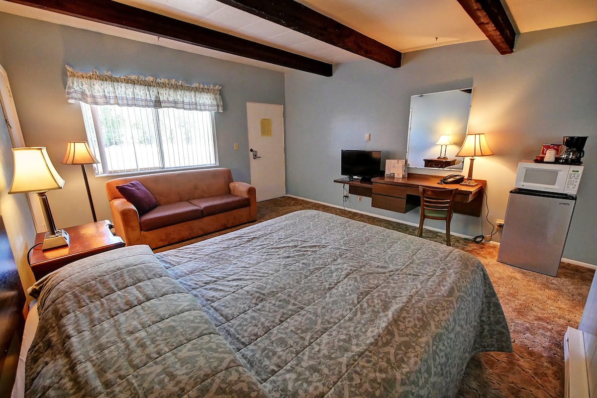 A bedroom with a bed, a desk, a chair, a television, a refrigerator, and a window with curtains.