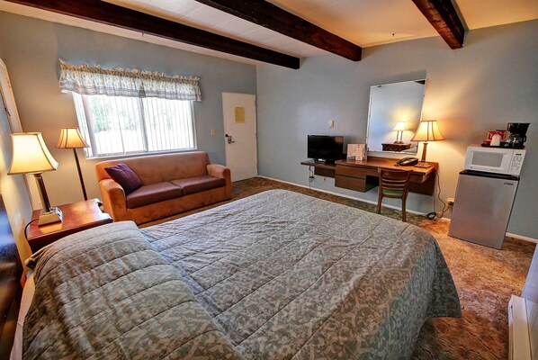 A bedroom with a bed, a desk, a chair, a television, a refrigerator, and a window with curtains.