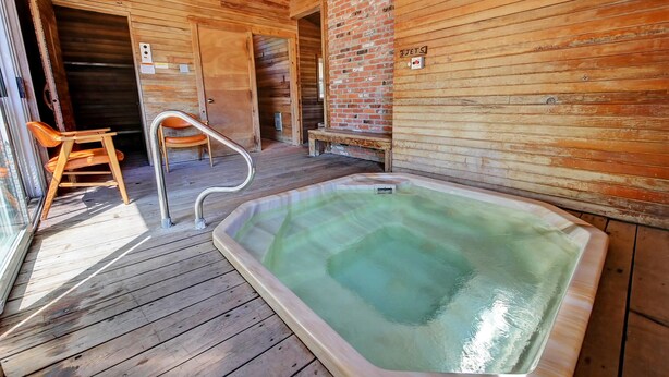 A wooden interior with a hot tub, wooden benches, and a chair near a glass door. - Idle A While (Twisp)